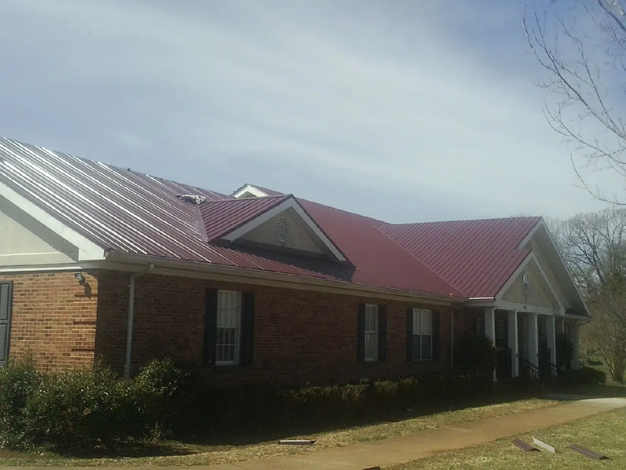 Red metal roof with gabled entries on a long brick building, from a Hail Damage Roof Repair job in Virginia City