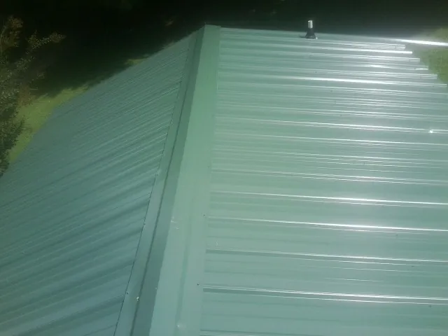 New green metal panels meeting at the ridge of a roof — Flat Roof Repair work by our crew in Virginia City